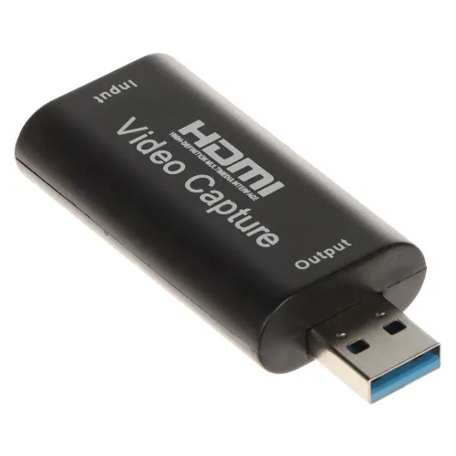 Na zdjęciu znajduje się czarny adapter USB oznaczony jako "HDMI Video Capture", z portami opisanymi jako "Input" i "Output". Adapter ma niebieskie złącze USB i jest przeznaczony do przechwytywania sygnału wideo.