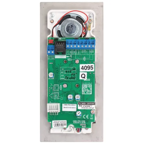 Zdjęcie przedstawia zieloną płytkę drukowaną z różnymi komponentami elektronicznymi, w tym złączami, przewodami i głośnikiem. Na płytce znajdują się oznaczenia techniczne oraz naklejki z numerami seryjnymi.