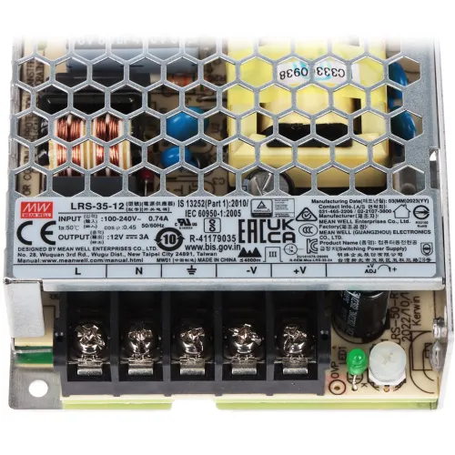 Zasilacz impulsowy z metalową obudową o strukturze plastra miodu, widoczny z góry z oznaczeniami technicznymi na etykiecie. Na dole znajdują się zaciski śrubowe do podłączenia przewodów.