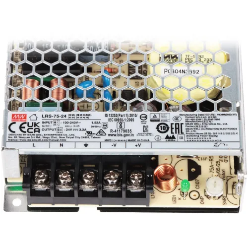 Zdjęcie przedstawia zasilacz impulsowy z widocznymi elementami elektronicznymi, takimi jak cewki i kondensatory, umieszczonymi pod metalową kratką. Na obudowie znajdują się oznaczenia techniczne i certyfikaty zgodności.