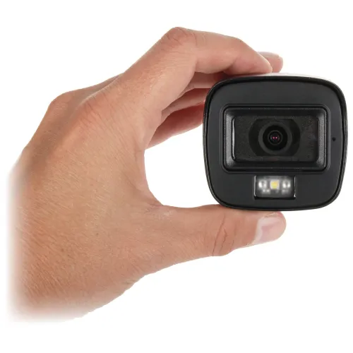 Na zdjęciu widać rękę trzymającą małą kamerę z obiektywem skierowanym w stronę widza. Kamera jest czarna i posiada wbudowane diody LED poniżej obiektywu.