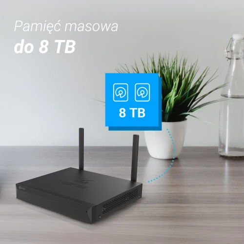 Na zdjęciu znajduje się czarny rejestrator IP Ezviz X5S-8W z dwoma antenami, umieszczony na drewnianym blacie. W tle widoczna jest zielona roślina w białej doniczce oraz szklana butelka, a w lewym górnym rogu znajduje się napis "Pamięć masowa do 8 TB".