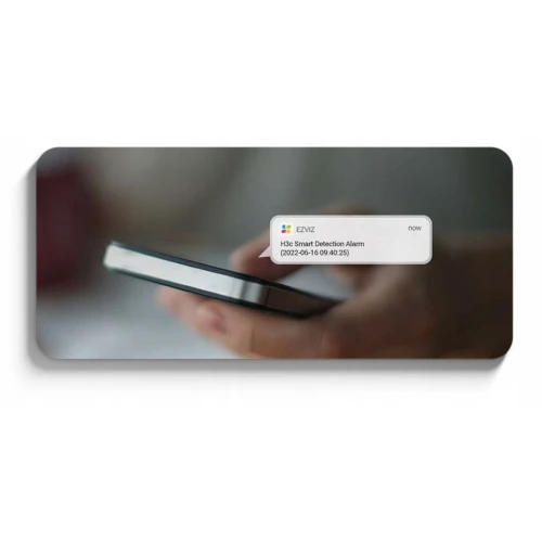 Osoba trzyma w dłoni smartfon, na którym wyświetla się powiadomienie o alarmie wykrytym przez kamerę EZVIZ. Powiadomienie zawiera datę i godzinę zdarzenia.