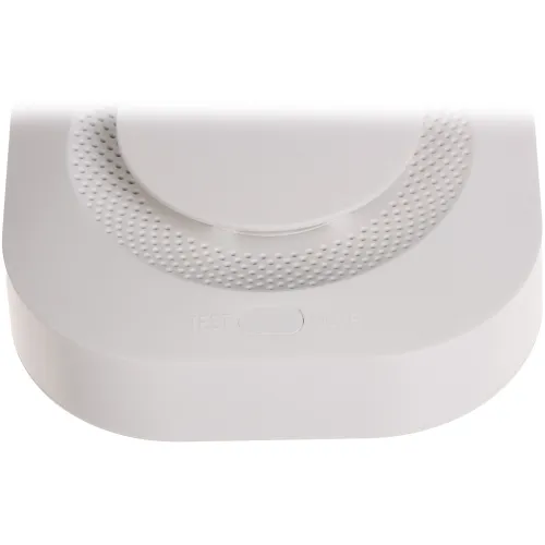 Zdjęcie przedstawia biały przycisk resetu na urządzeniu z teksturą w postaci małych wypustek wokół przycisku. Na obudowie widoczne są napisy "TEST" i "MUTE".