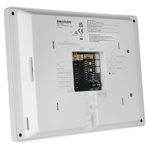 Zdjęcie przedstawia tylną część białego wideodomofonu z widocznymi złączami i oznaczeniami technicznymi. Urządzenie ma prostokątny kształt i jest wyposażone w kilka portów do podłączenia kabli.