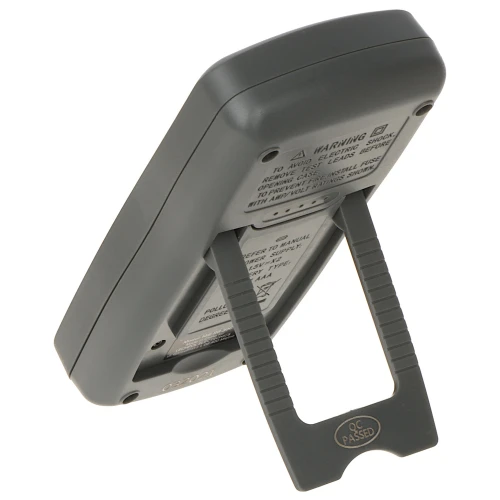 Na zdjęciu widoczny jest tył przenośnego urządzenia elektronicznego z wysuwaną podpórką, umożliwiającą ustawienie go pod kątem. Obudowa jest w kolorze ciemnoszarym, a na tylnej części znajdują się etykiety z ostrzeżeniami i certyfikatem jakości.